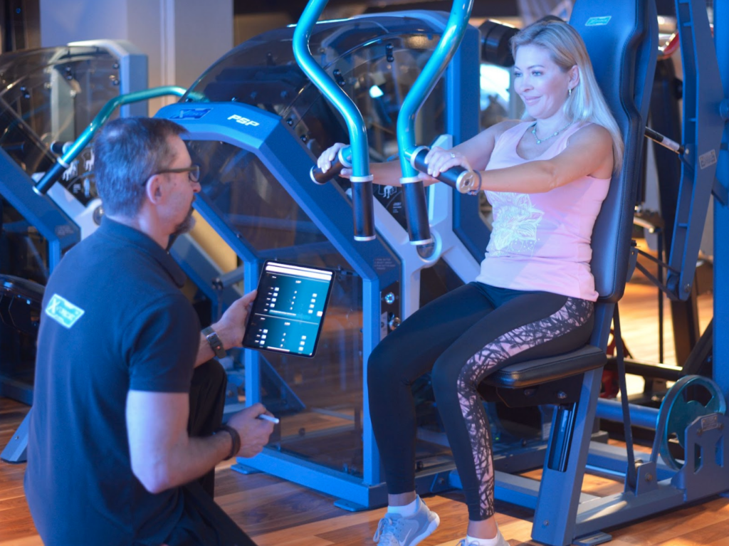 Male personal trainer at X-force guides a woman in the gym